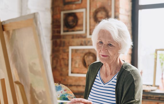 Elderly woman paints in a light-filled room