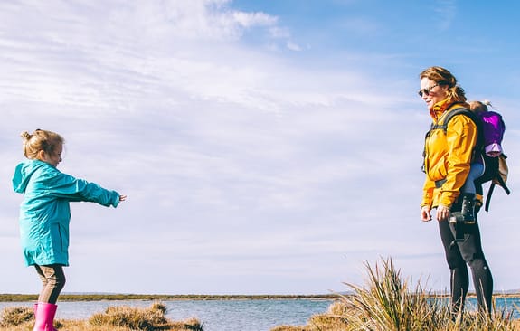 Mother and daughters in bright coats walking along a lake