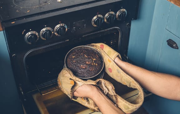 Slightly burnt cake being pulled out of a rustic oven