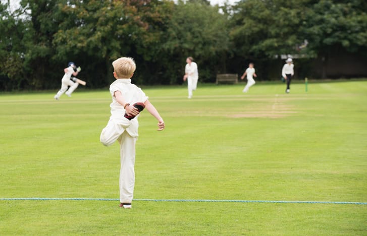 Child in cricket whites stretching in the outfield during a match