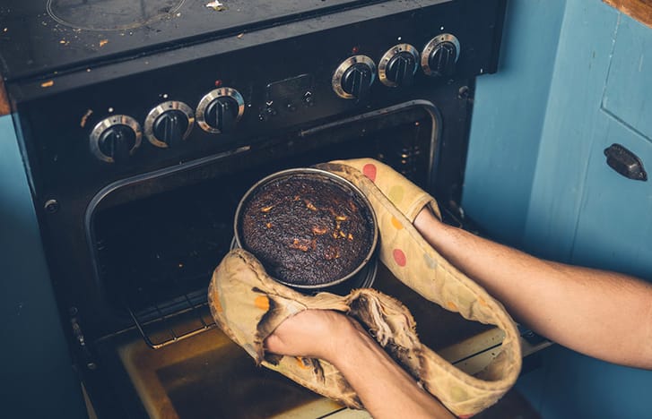 Slightly burnt cake being pulled out of a rustic oven