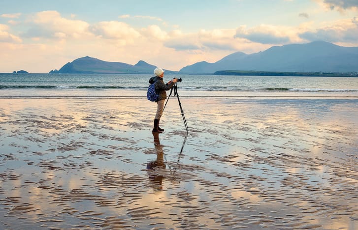 Photographer with a tripod capturing a still beach at sunset