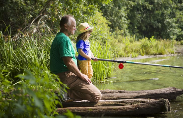 Man fishing in a river with his granddaughter