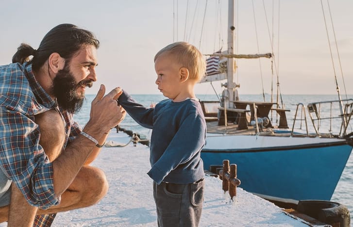 Man in dockyard bends down to attend toddler