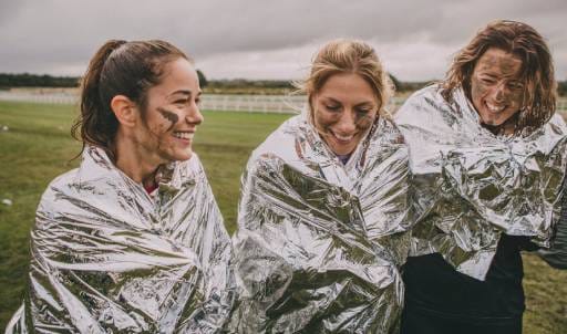 Three women wearing space blankets embrace after completing a charity sporting event