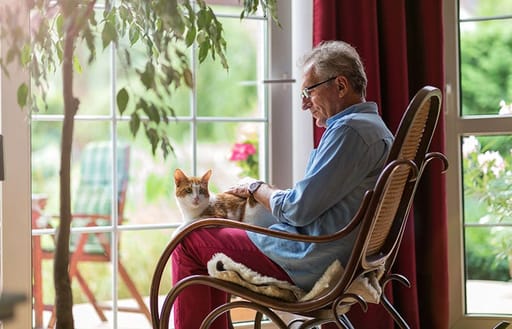 A man sits in a chair while patting his cat