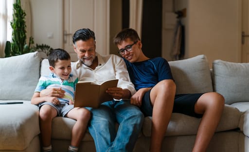 A father reads a book with his young sons on a sofa at home
