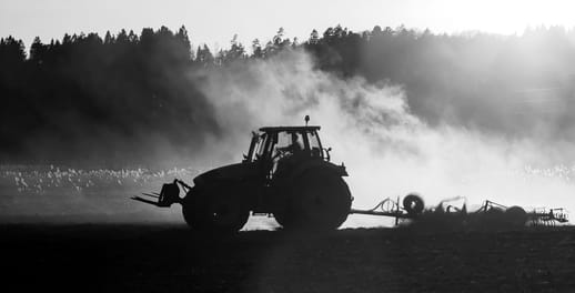 A tractor ploughs a field, generating dust