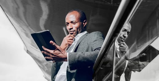 Close up of a business man looking at tablet leaning against glass railing outside office