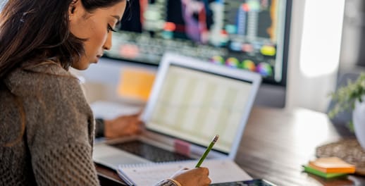 Young woman tracking and trading stocks using laptop and desktop computer