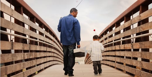 Father and son carrying fishing rods walking over a wooden bridge