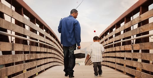 Father and son carrying fishing rods walking over a wooden bridge