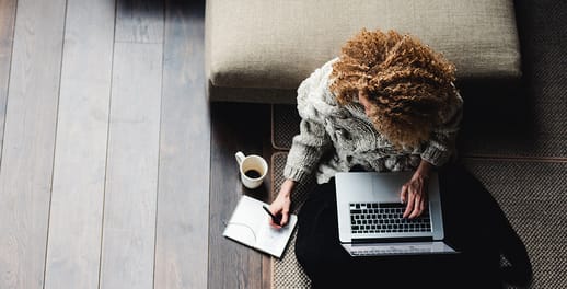 Aerial view of curly-haired lady working on laptop with a coffee