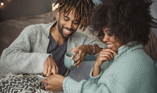 Couple sitting on sofa with a cup of tea and checking mobile phone