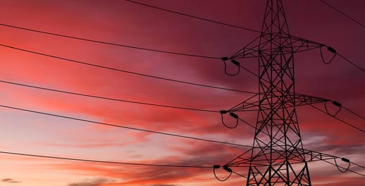 An electricity transmission tower stands tall with a red sunset in the background