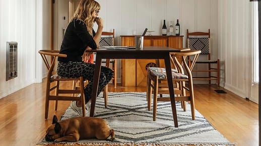 Woman sitting at a table in her house with dog at her feet