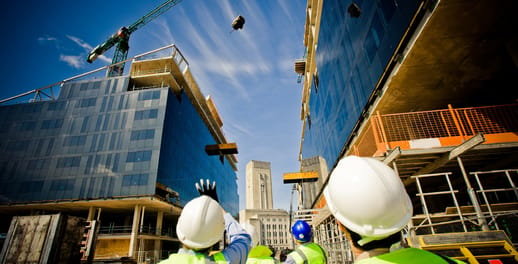 builders watching a crane carrying equipment over high rise buildings