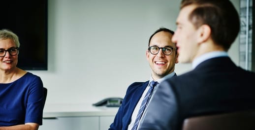 A woman and two men in corporate dress speak at a meeting around a boardroom table