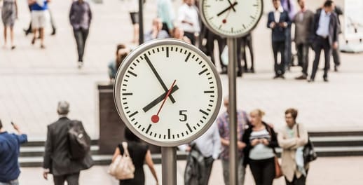 People walk under the Canary Wharf clocks