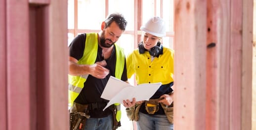 Two builders looking at drawings inside the timber frame of a new house