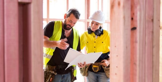 Two builders looking at drawings inside the timber frame of a new house