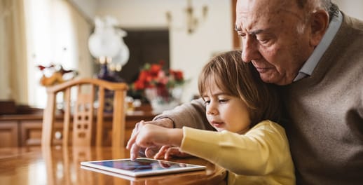 An elderly man looking at his tablet with his grandchild