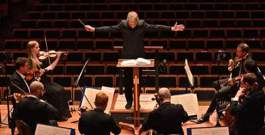 The conductor of the Bournemouth Symphony Orchestra conducts the orchestra, with arms stretched