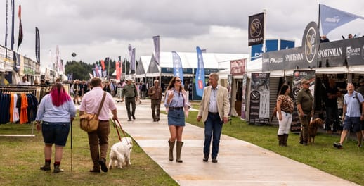 People and dogs walking down the main walkway of the Game Fair, with stalls either side