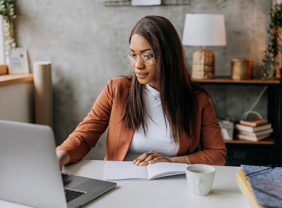 Business woman wearing a rust blazer working on laptop