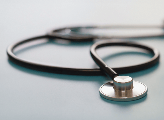 Hand holding stethoscope alongside computer screen