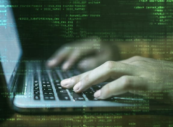 Cybersecurity: hacker's hands on keyboard with computer code in background