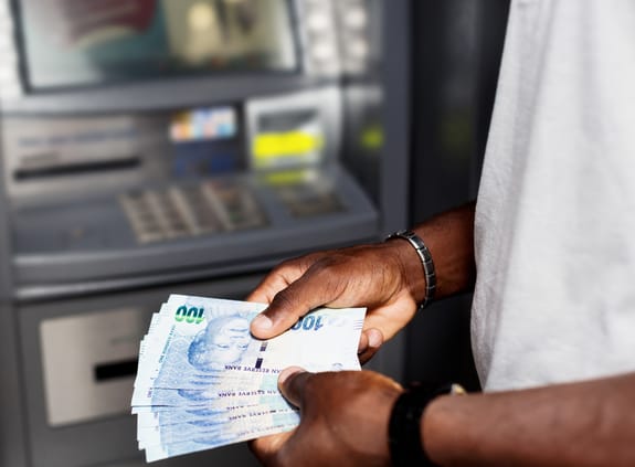 Man holding rand notes alongside an ATM