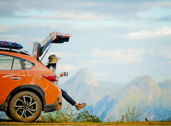 Woman sitting in the boot of her car looking out at a mountainous view 