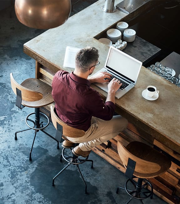 male working on laptop at a restaurant counter with a coffee