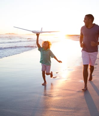 Travel | Son and father playing on a beach with an aeroplane