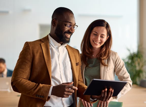 Business man and business woman chatting in meeting room looking at tablet