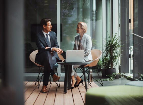 Business man and business woman chatting at a coffee table with laptop