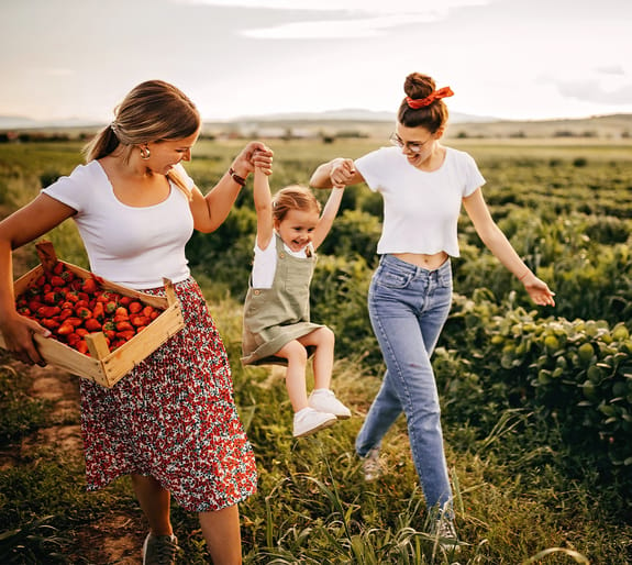 two females swining a young girl while walking through strawberry field