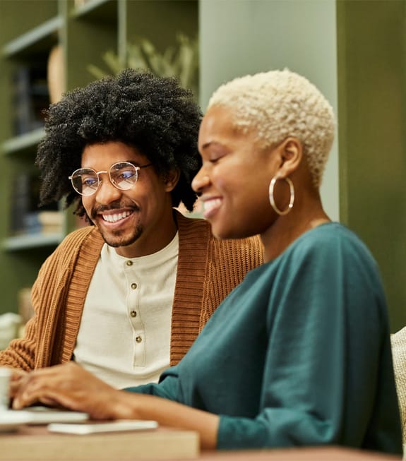 My Investments | couple smiling while sitting at a table and looking at their digital investment platform