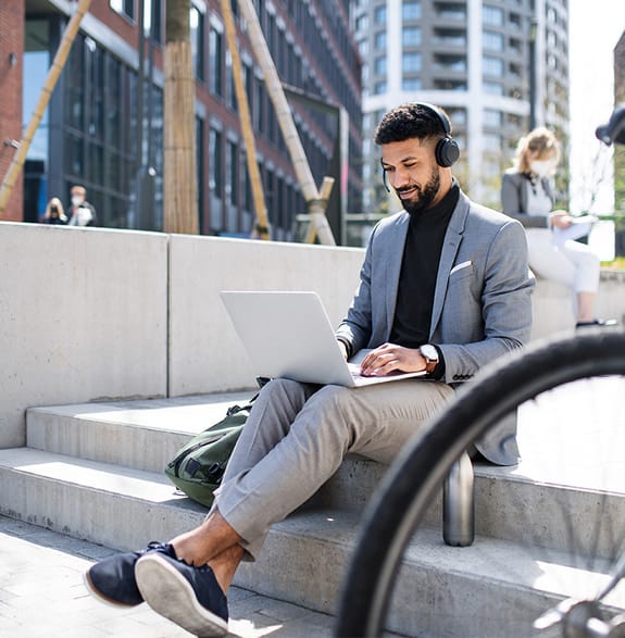 Business man sitting on his laptop working on his digital investment platform on a step outdoors with a bicycle next to him 