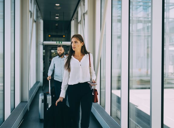 Business colleagues pulling luggage while walking in corridor at airport