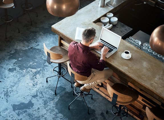 male working on laptop in a restaurant with a coffee