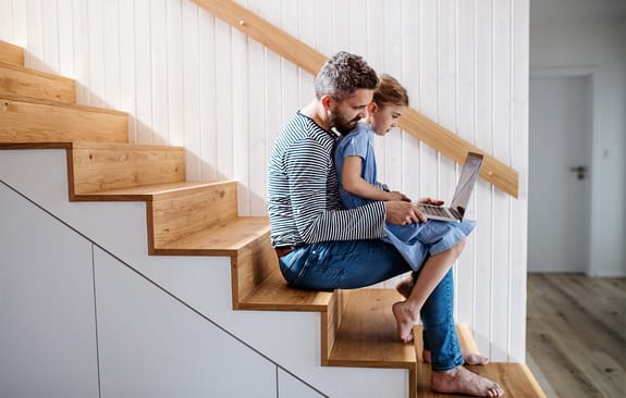 Dad and daughter sitting on stairs looking at a laptop