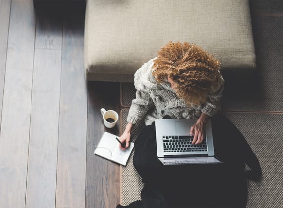 female working on laptop sitting on the floor at home