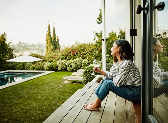 Smiling woman enjoying glass of wine while watching sunset from backyard