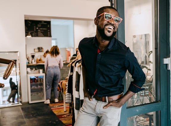 Smiling business owner with hands in pockets standing at doorway of clothing store