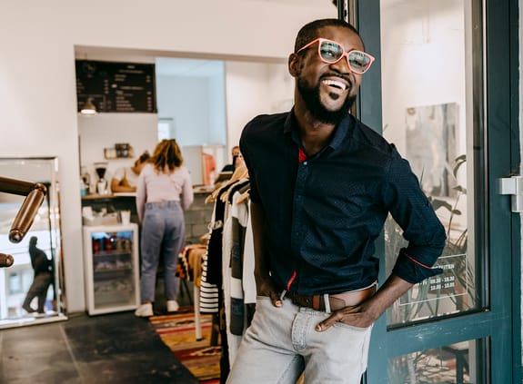 Smiling business owner with hands in pockets standing at doorway of clothing store