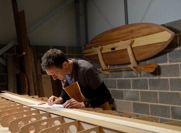 Man using small metal ruler while making wooden paddleboard in workshop
