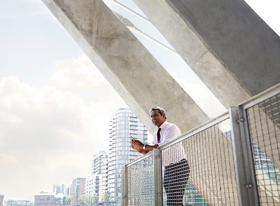 businessman standing on a balcony with building structure behind him along with city skyline
