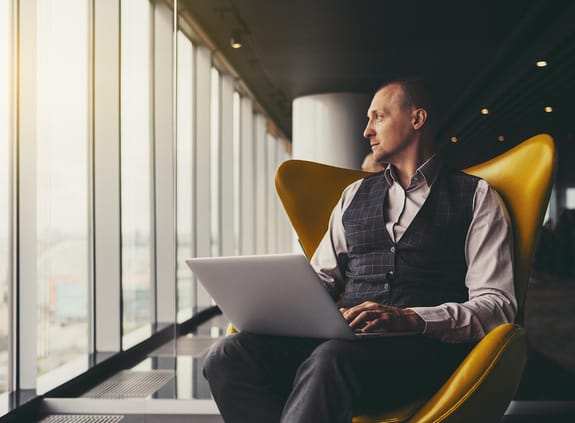 Man on a computer in a business lounge looking out the window